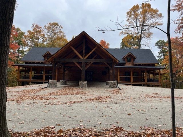 Log cabin with a covered entrance, set in a wooded area with autumn foliage.