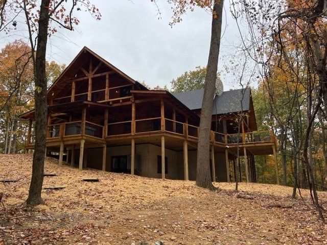 Wooden cabin on stilts in autumn forest with screened-in porches and a dark roof.