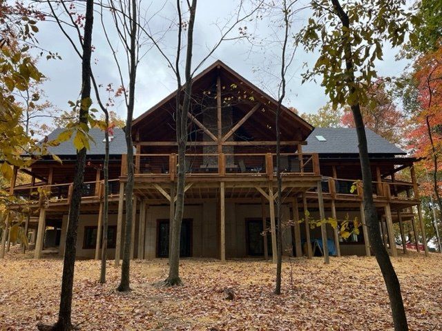 A two-story wooden cabin with a wraparound porch, surrounded by trees with fall foliage.