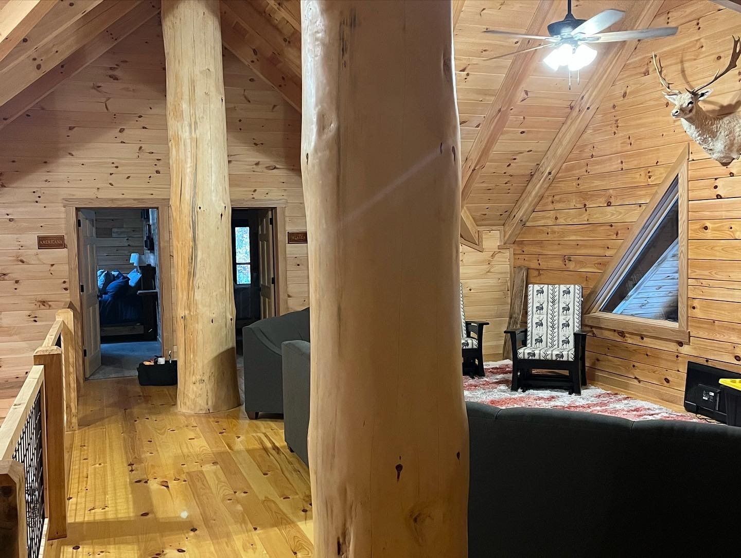 Wooden cabin interior with exposed beams, a loft, and natural wood furnishings.