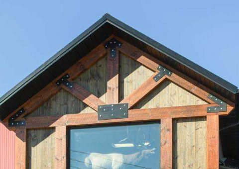 Wooden building facade with dark roof, decorative beams, and large window.