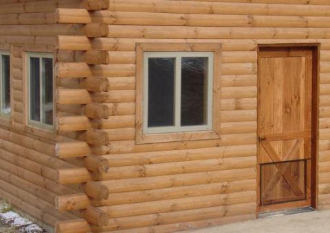 Log cabin exterior with light brown logs, windows, and a door.