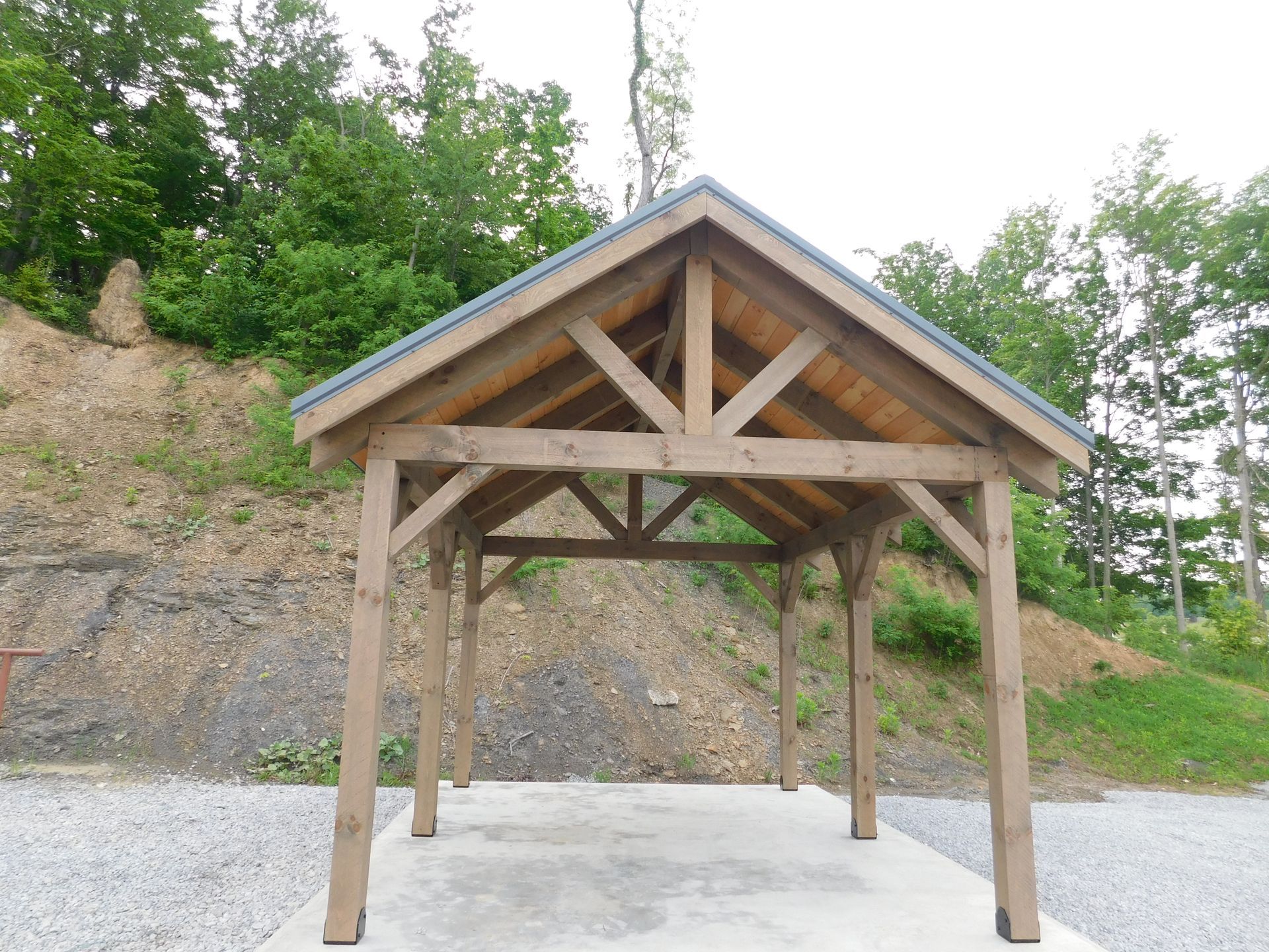 Wooden pavilion with a gray roof in a natural setting.