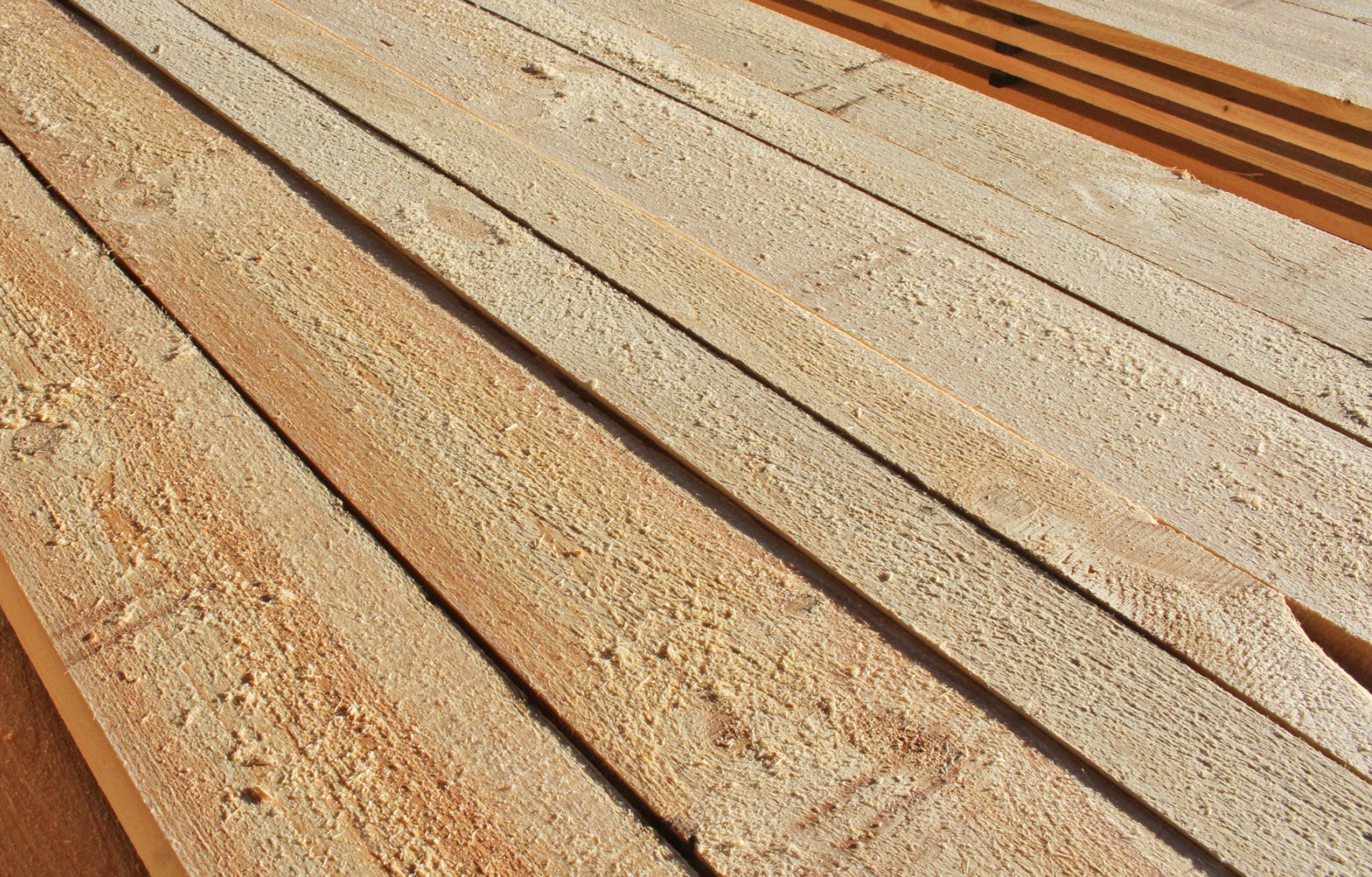Wooden planks, light brown, stacked. Close-up view of the surface grain.