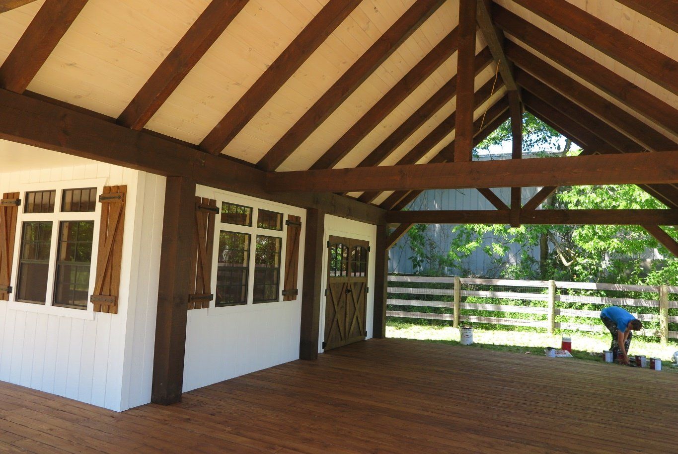 Wooden-framed pavilion with brown beams, white walls, and wood deck. A person kneels outside.