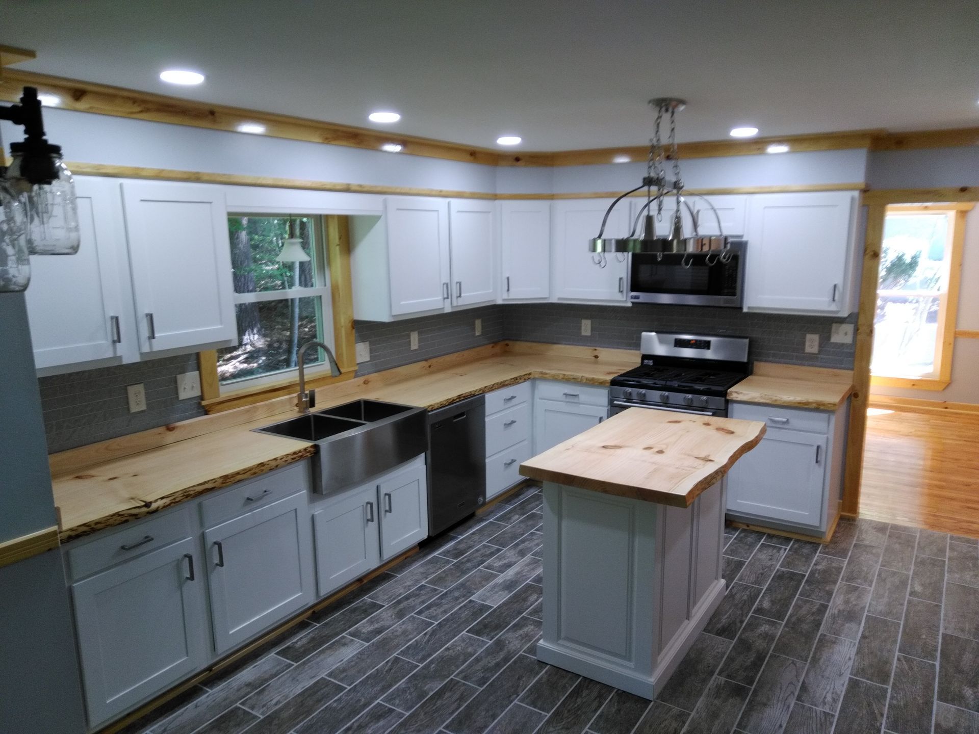 Kitchen with white cabinets, wood countertops, island, stainless steel appliances, and gray tiled floor.