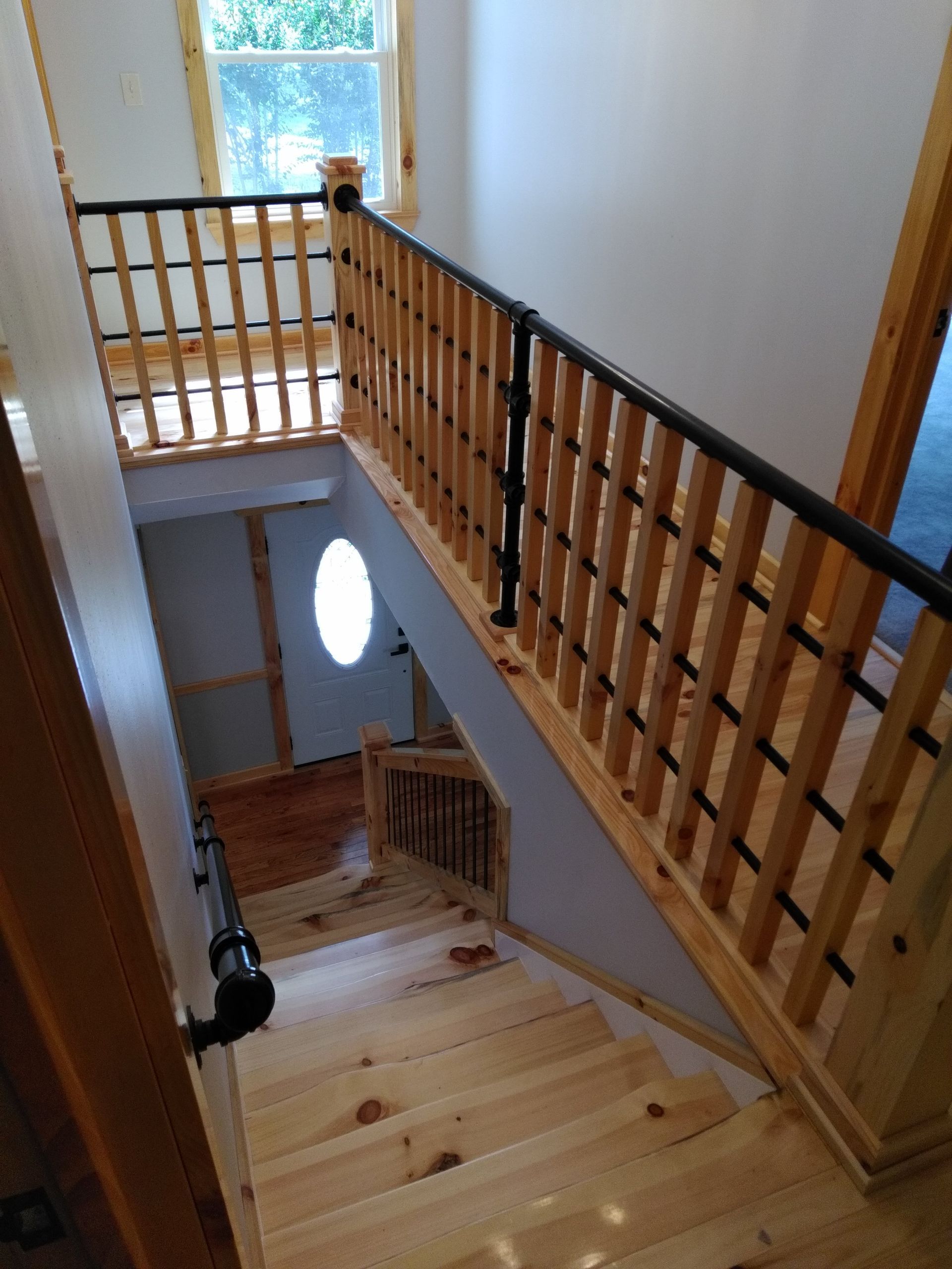 Wooden staircase with black railings, leading downward. Sunlight streams through a window.