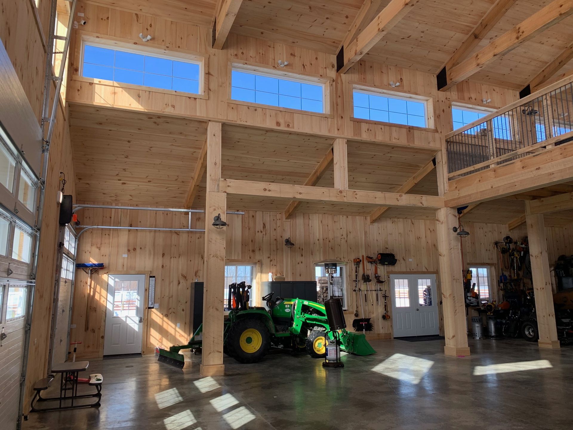 Interior of a large wooden building with a green tractor, high ceilings, and windows.