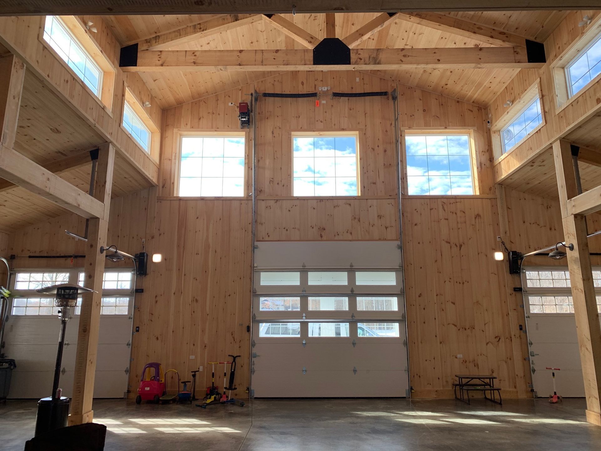 Interior of a light-filled wooden garage with a high ceiling, windows, and three garage doors.