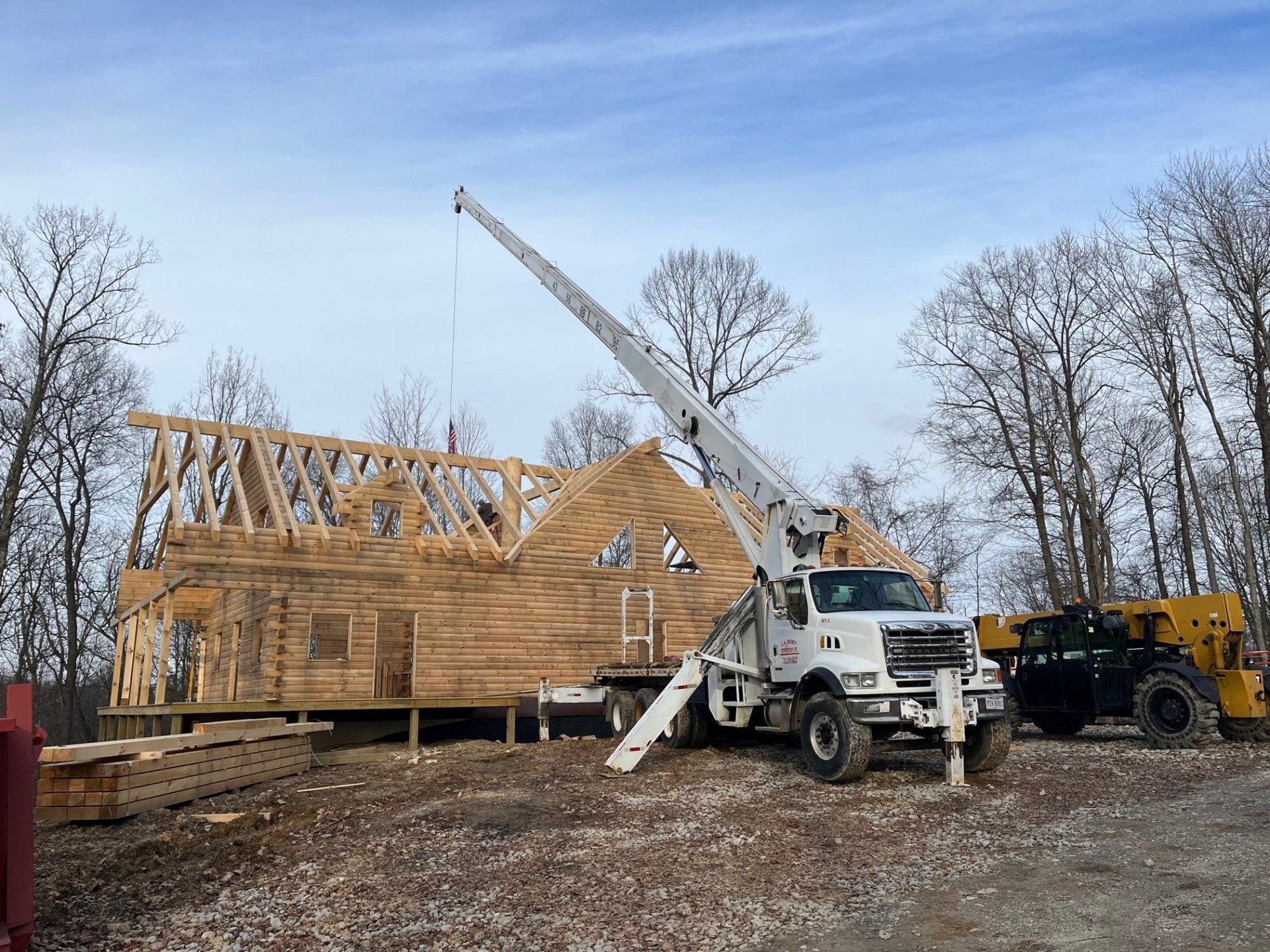 Log cabin under construction, crane lifting building materials.
