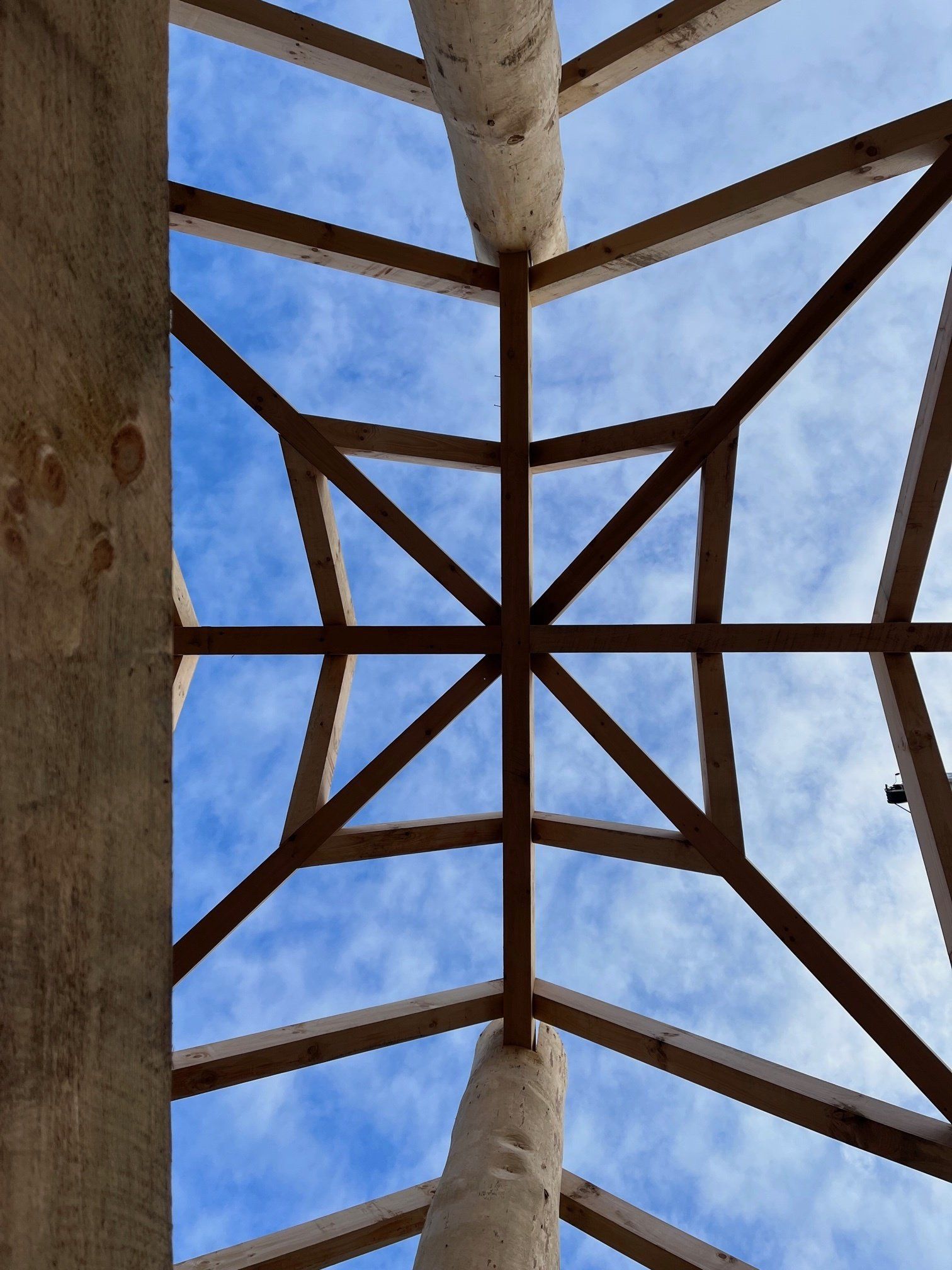 Wooden beams forming a geometric pattern against a blue sky, framing an opening.