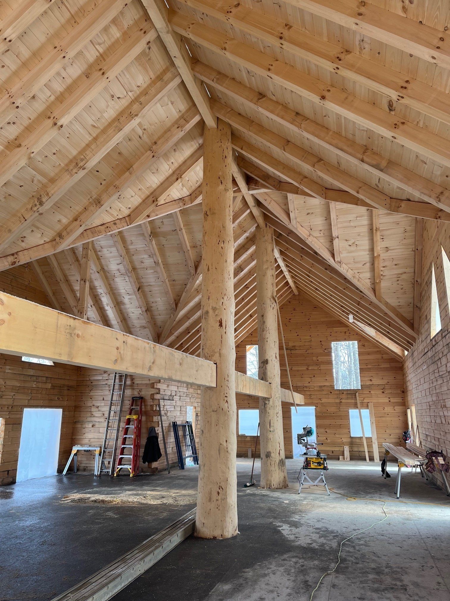 Interior view of a wooden building under construction, showing rafters, beams, and support posts.