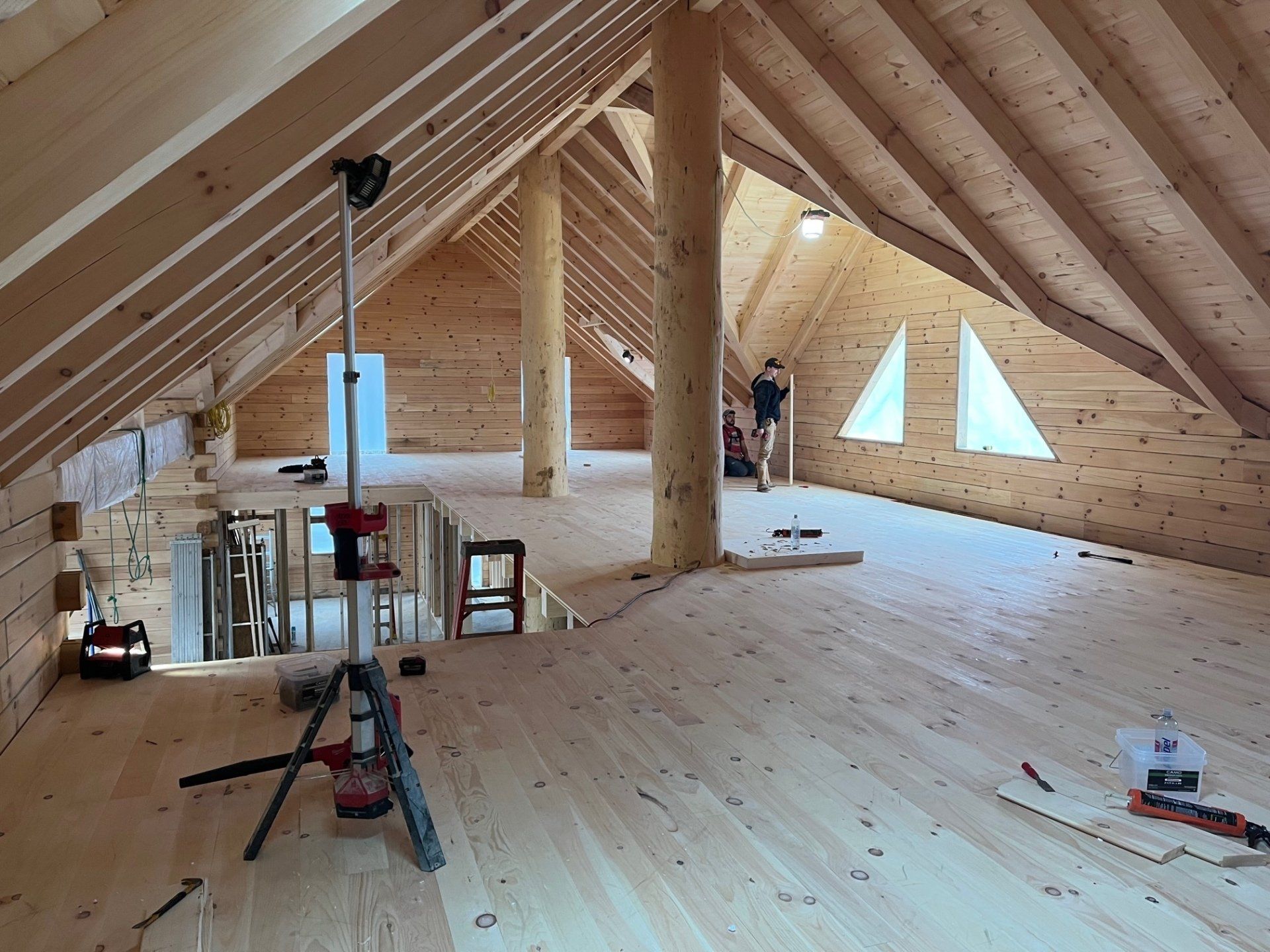 Interior of a wooden attic under construction. A person stands near small windows.