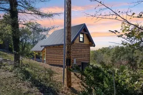 Small cabin with a metal roof on a hillside at sunset; power pole in foreground.