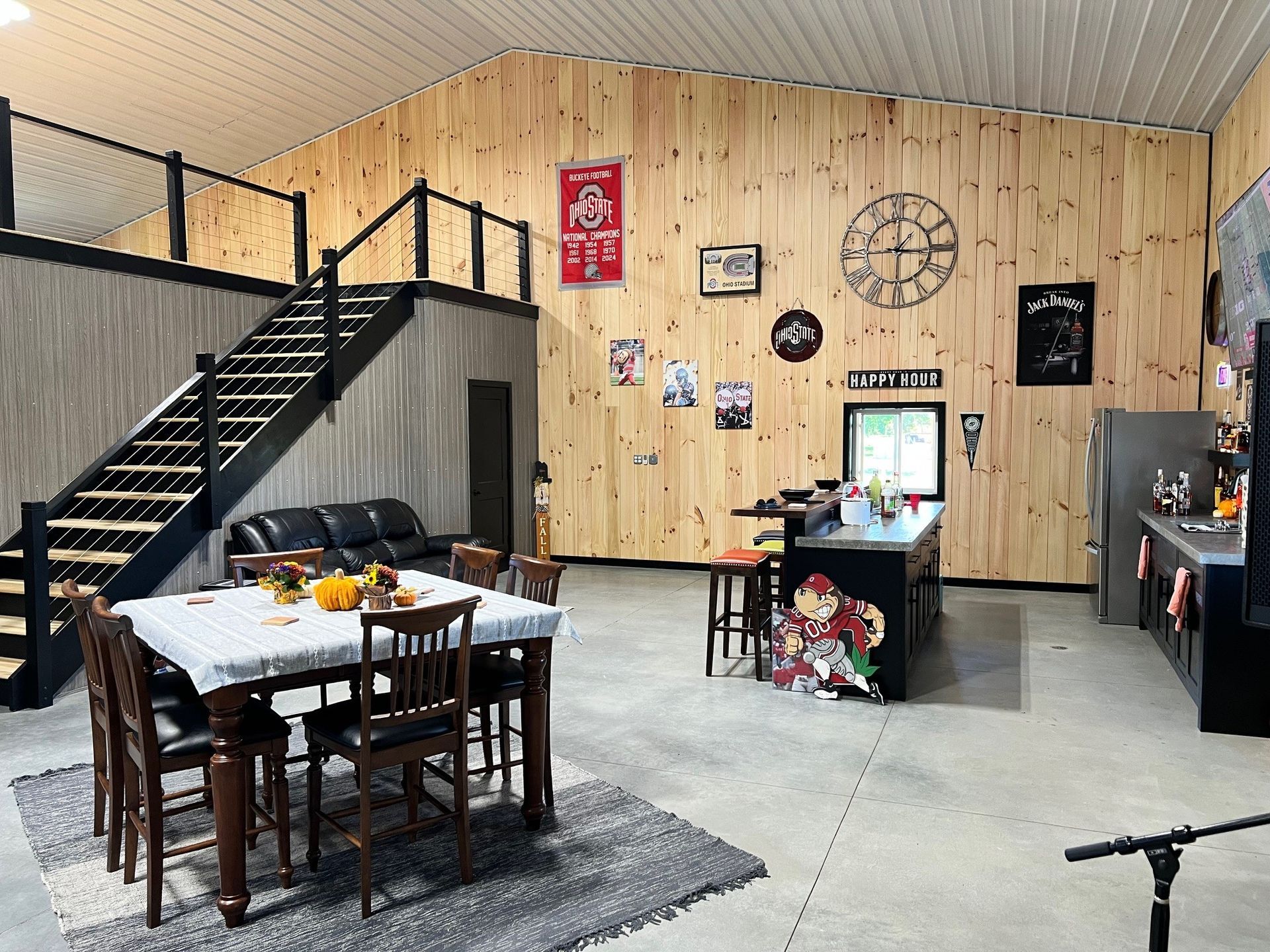 Interior of a large room with a kitchen, dining area, and mezzanine. Wooden walls, concrete floor, sports decor.