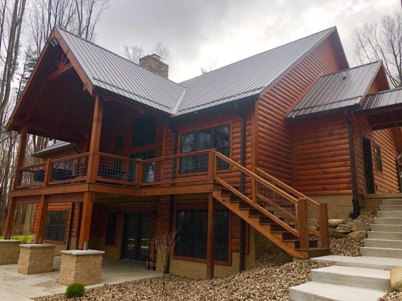 Log cabin with a metal roof, two-story wooden deck, and concrete steps leading to the entrance.