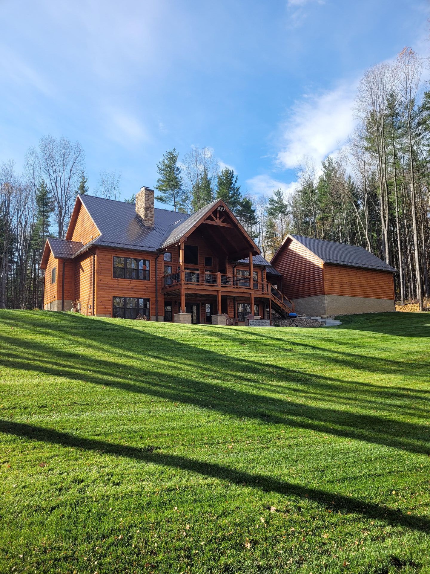Wooden cabin-style house with green lawn, trees, and blue sky.