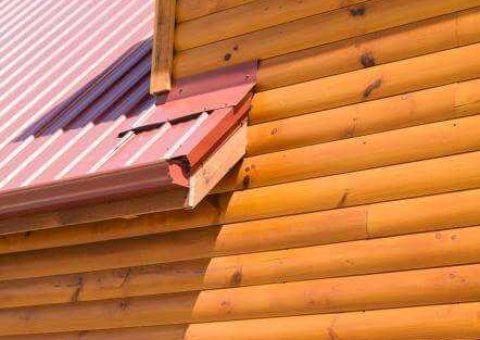 Red metal roof corner on a wooden log cabin wall.