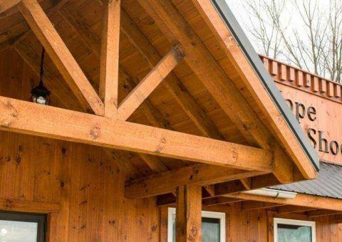 Wooden porch with a truss support, attached to a brown wooden building.