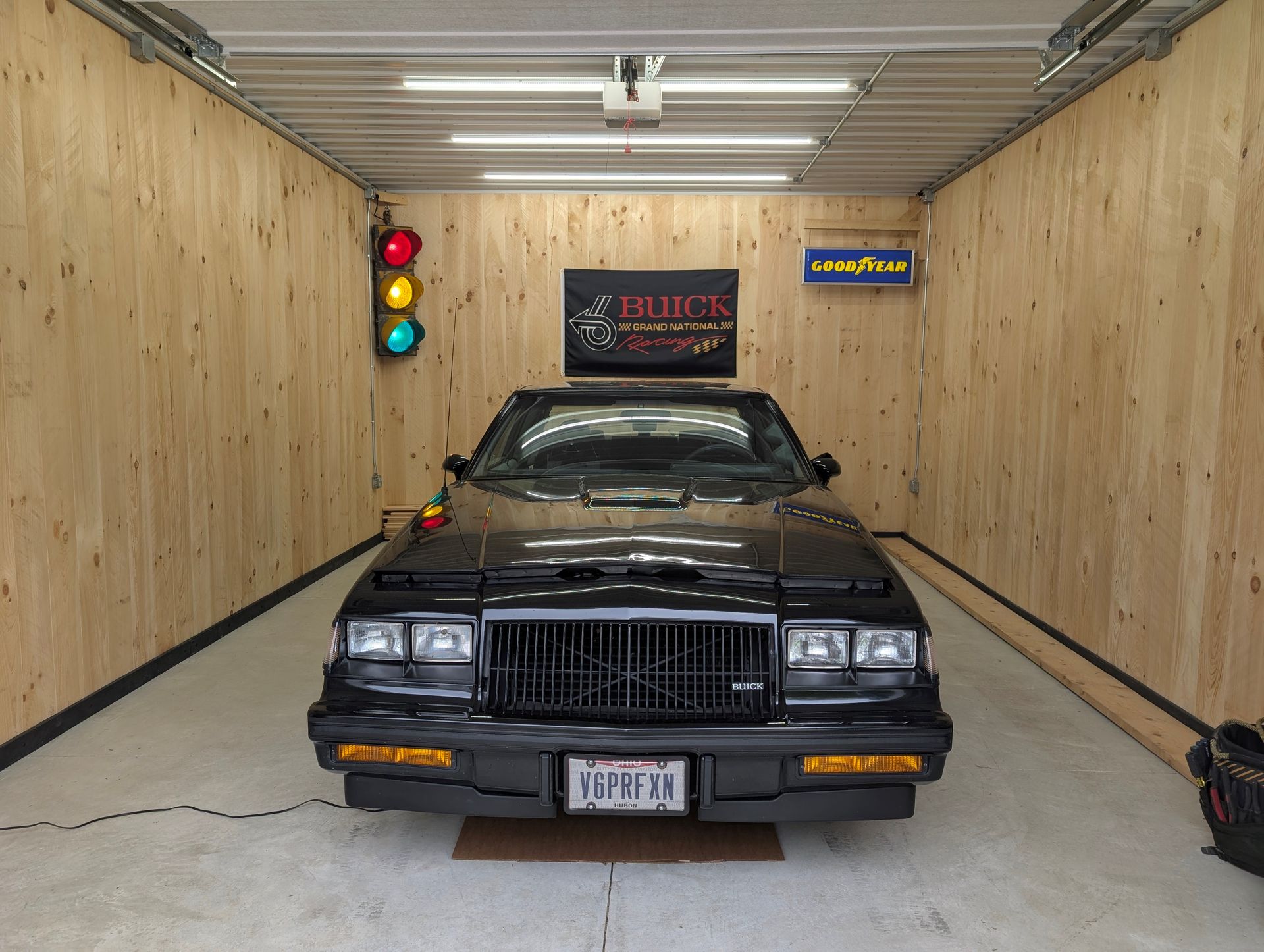 Black Buick Grand National in a wood-paneled garage with a traffic light.