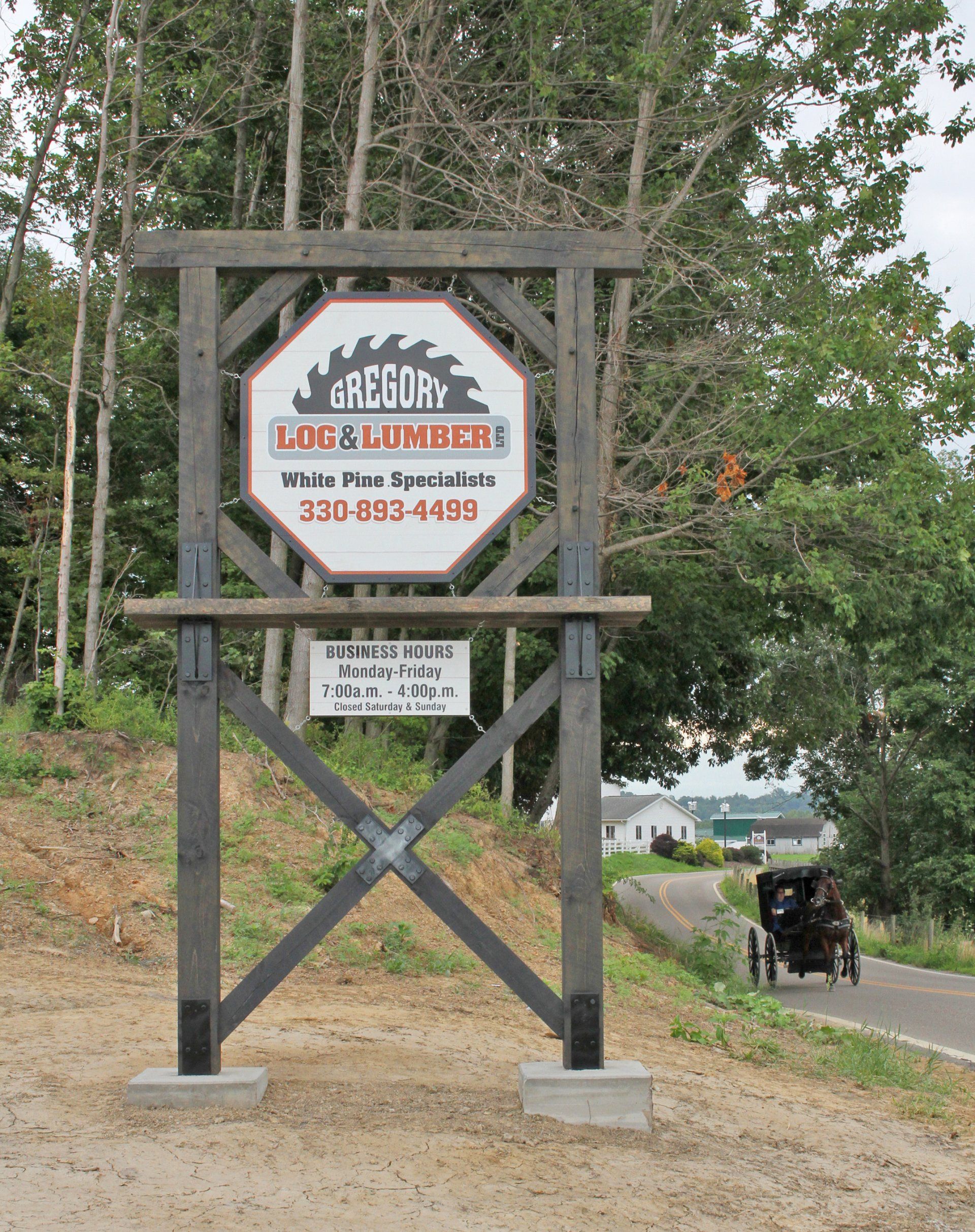 Sign for Gregory's Log Lumber with a saw blade logo, Amish buggy passing by on a road.