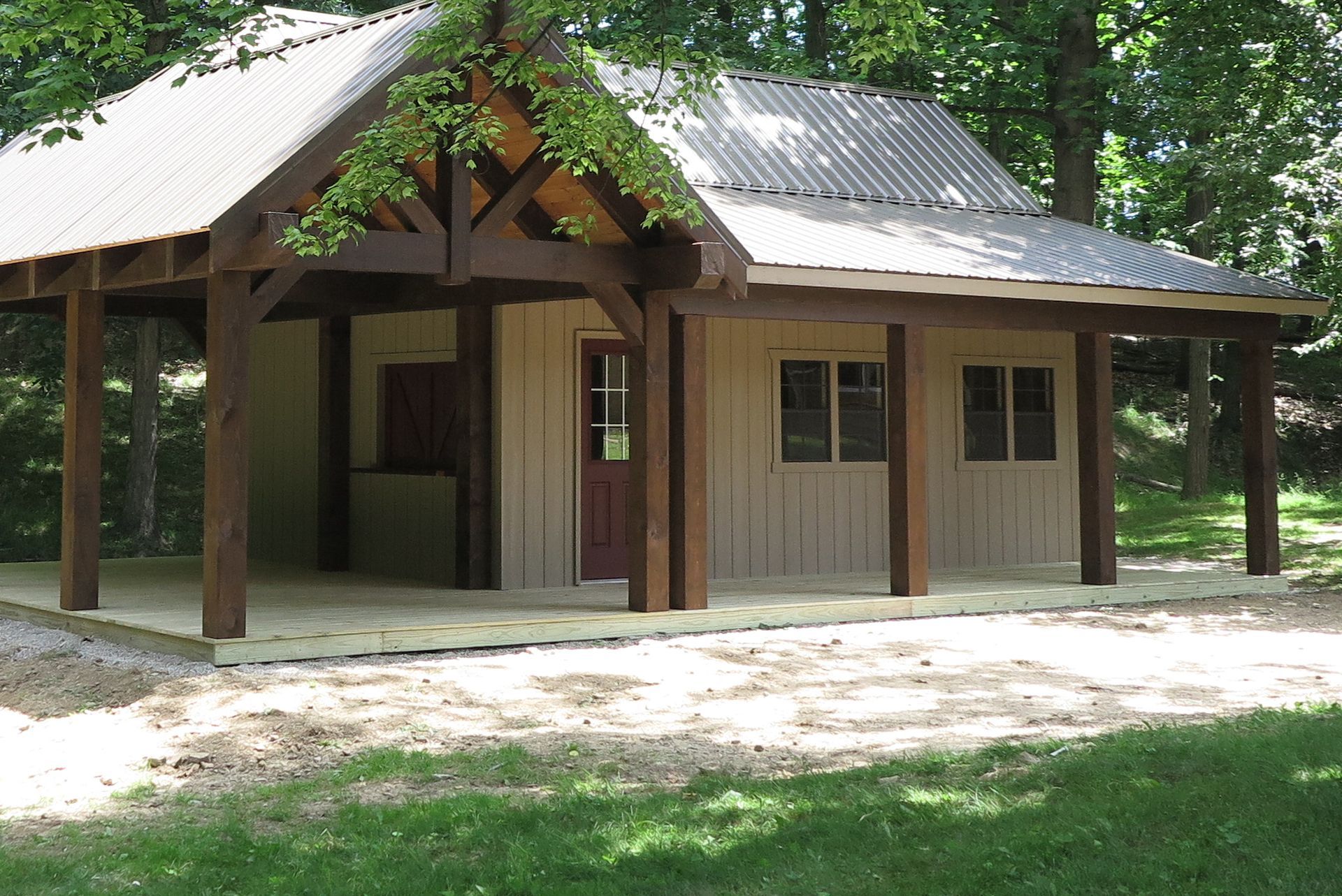 Small beige cabin with a covered porch and corrugated metal roof in a wooded area.
