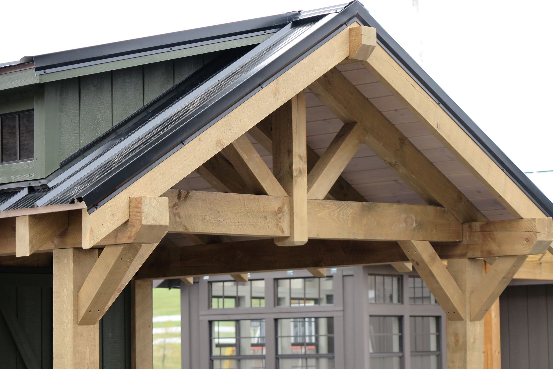 Wooden porch roof with black metal roof, green siding, and window.