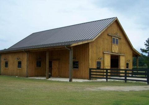 Wooden barn with a metal roof on a grassy field, under a cloudy sky.