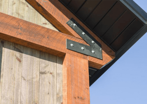 Wooden beams joined with a metal bracket at a building corner.