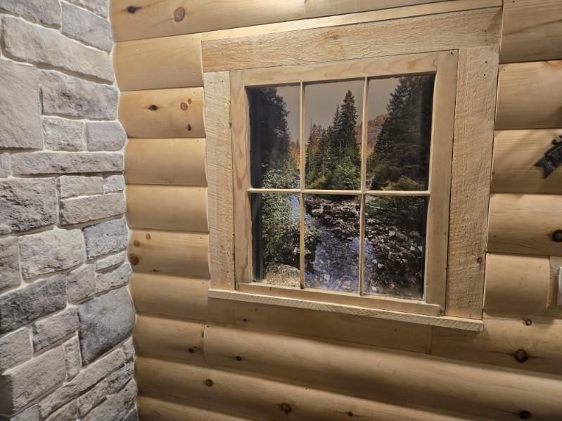 Log cabin interior with faux window displaying a forest scene; stone wall on left.