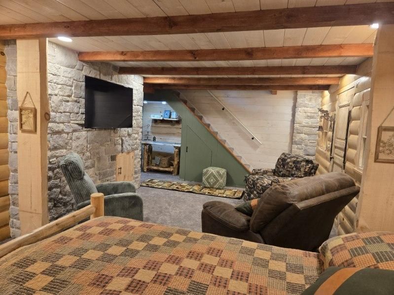 Cozy basement with stone walls, exposed beams, and comfortable seating around a TV.