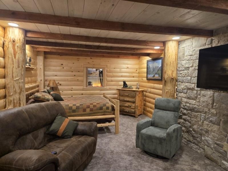Cozy log cabin bedroom with a bed, recliner, couch, and stone accent wall.