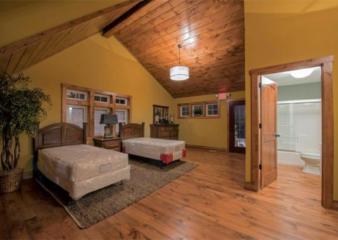 Bedroom with two twin beds, hardwood floor, yellow walls, wooden ceiling, and an open door to a bathroom.