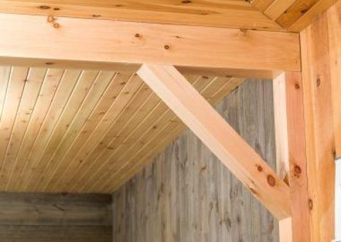 Wooden interior with a beam and angled support, wood-paneled ceiling and wall.