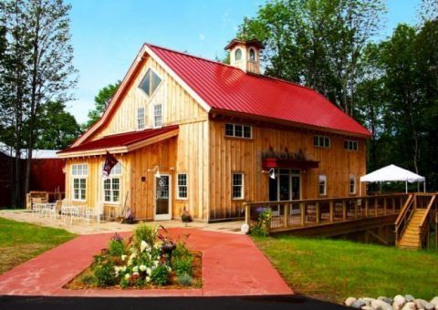 Wooden barn with red roof and small cupola, outdoor patio, red walkway, and green lawn.
