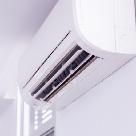 Unidad exterior de aire acondicionado con rejilla metálica en la parte superior y laterales ventilados de color gris.