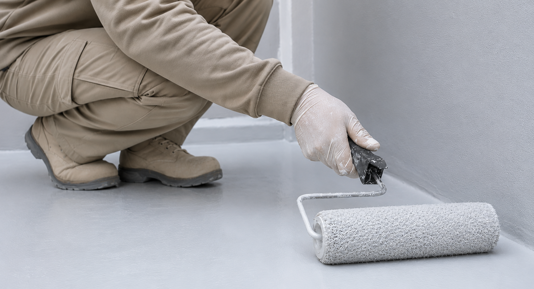 Una mano enguantada pinta una pared blanca con un rodillo sujeto a un mango naranja.