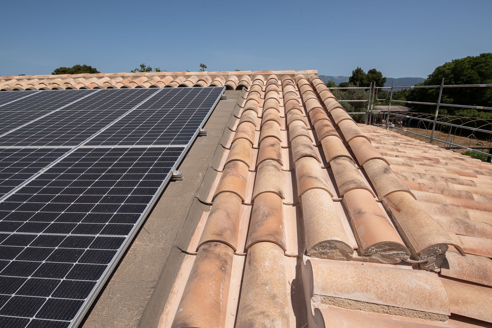 Paneles solares instalados a lo largo de un tejado de tejas de terracota bajo un cielo despejado.