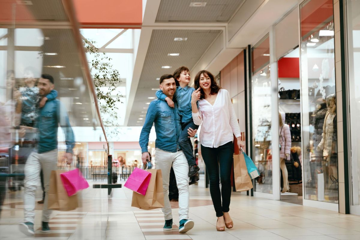A family is walking through a mall with shopping bags.