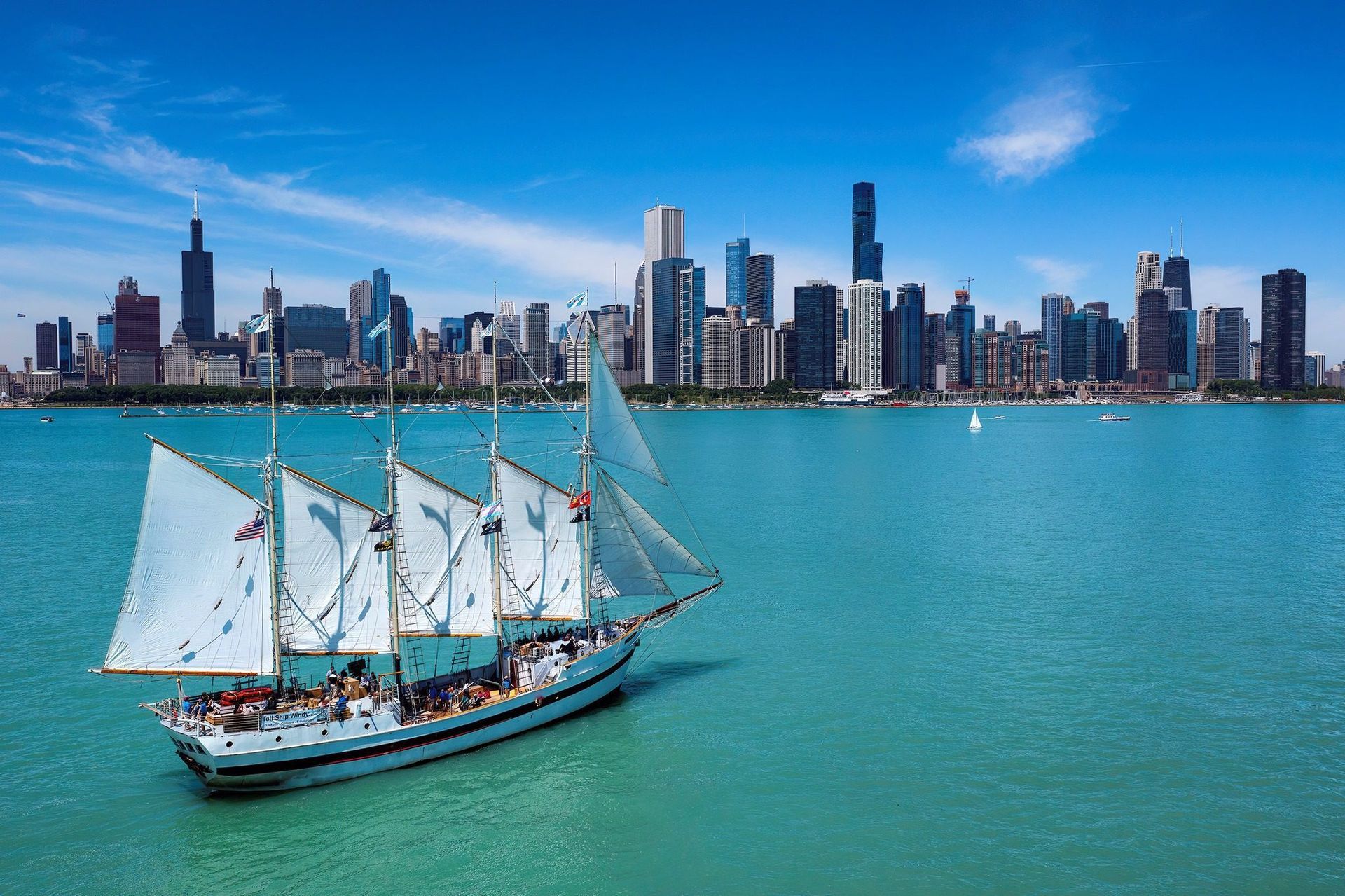 A sailboat is sailing in the water with a city skyline in the background.