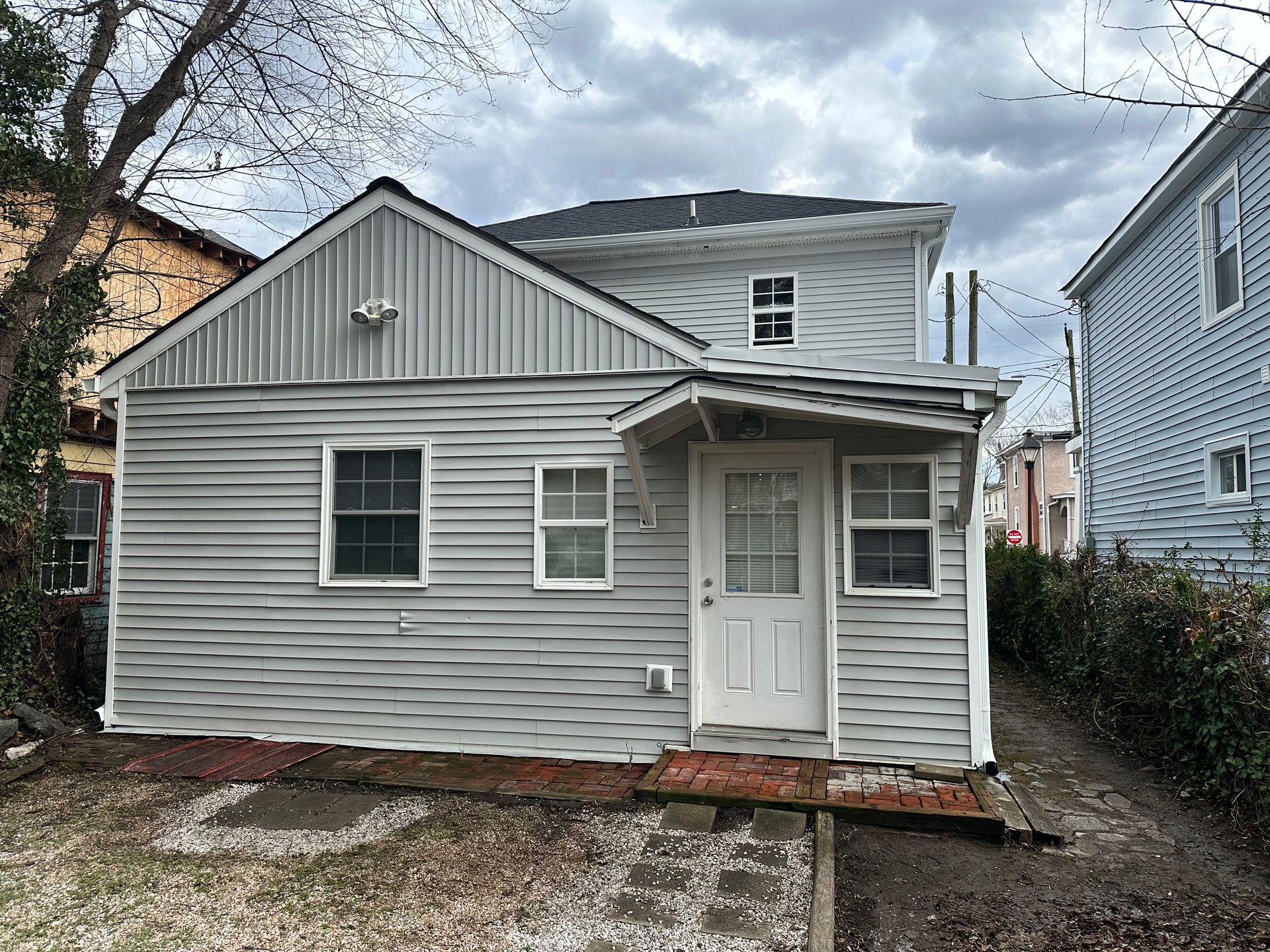 Back view of a two-story house with grey vinyl siding, white trim, a small covered entry, and a gravel-covered yard.