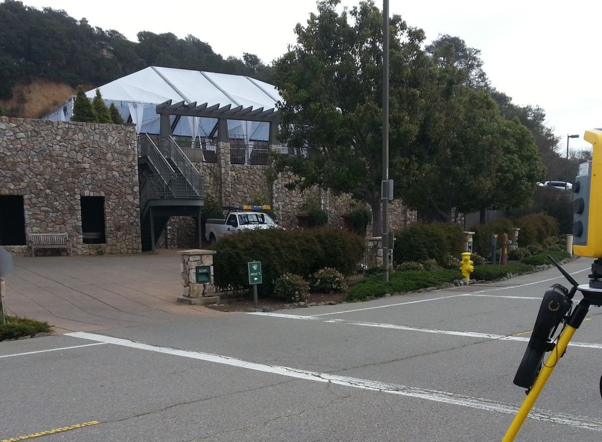 Yellow laser scanner on tripod, roadside, scanning a residential area.