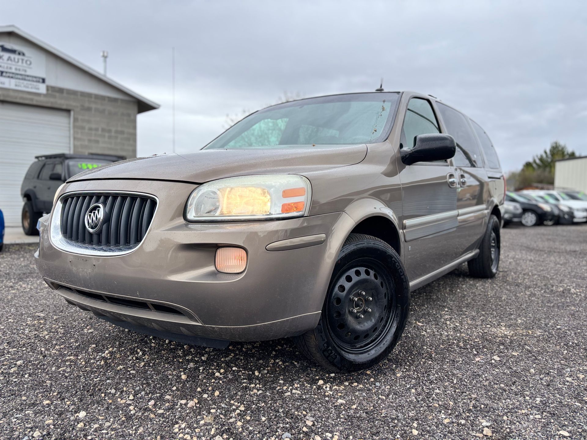 Beige Buick minivan parked on a gravel lot under a cloudy sky