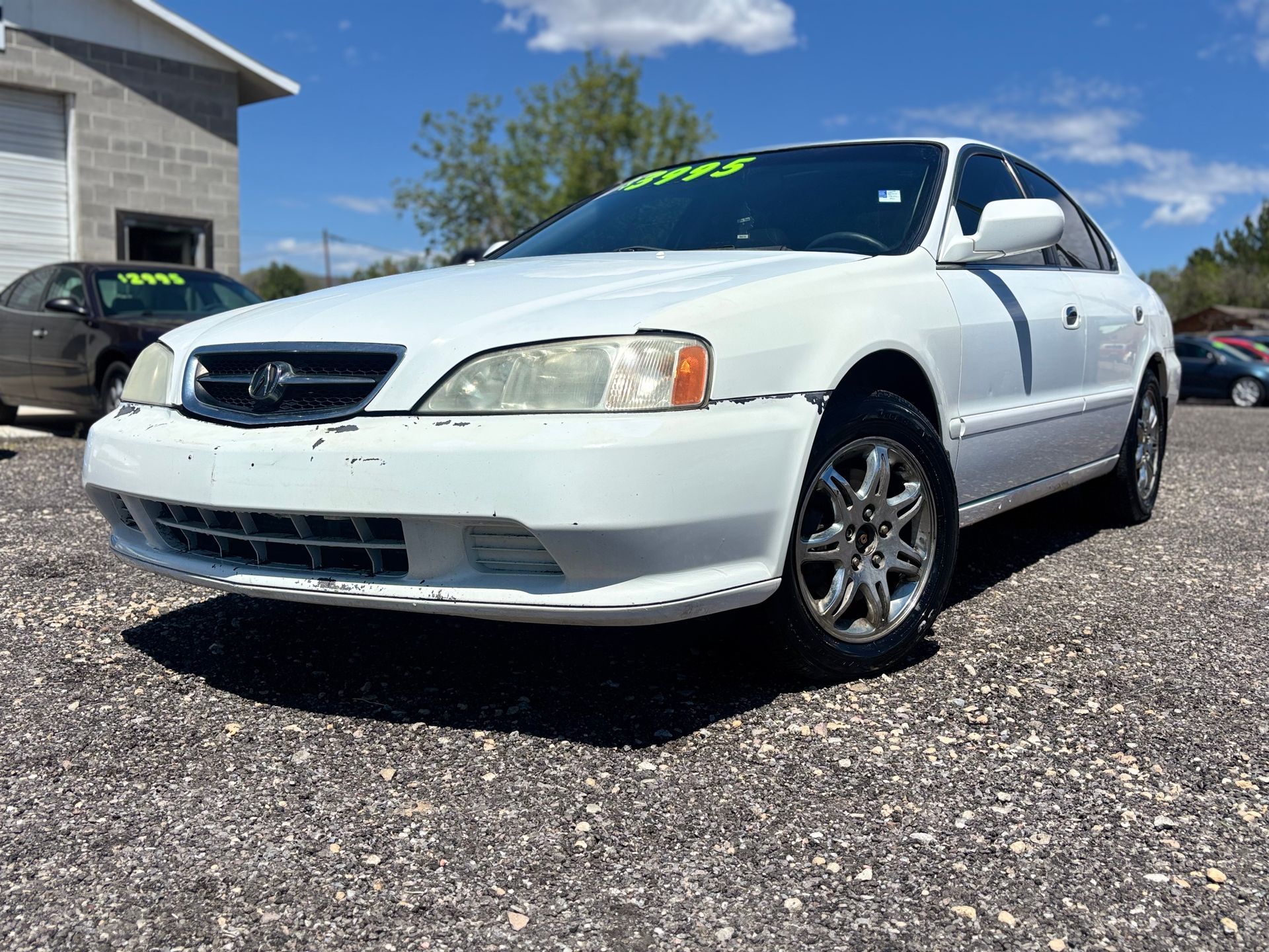White sedan parked on a gravel lot under a blue sky, viewed from the front-left side.