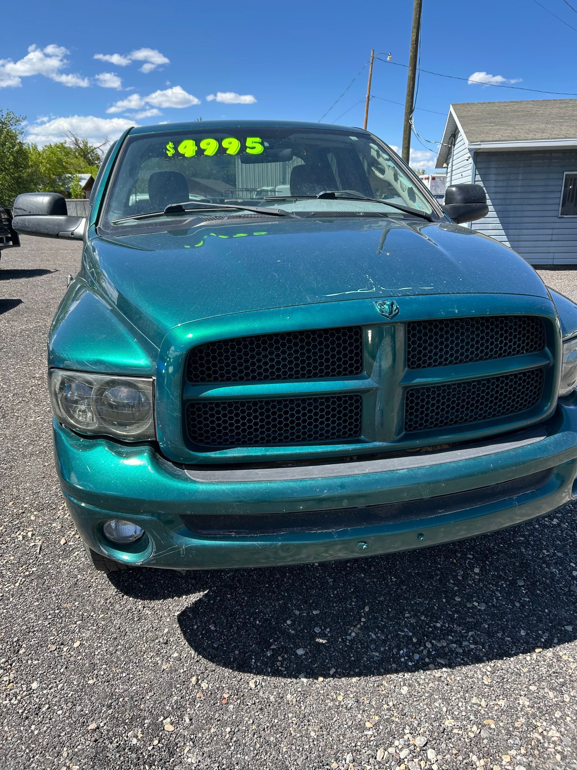 Teal Dodge pickup truck parked on gravel with a bright yellow price sign on the windshield