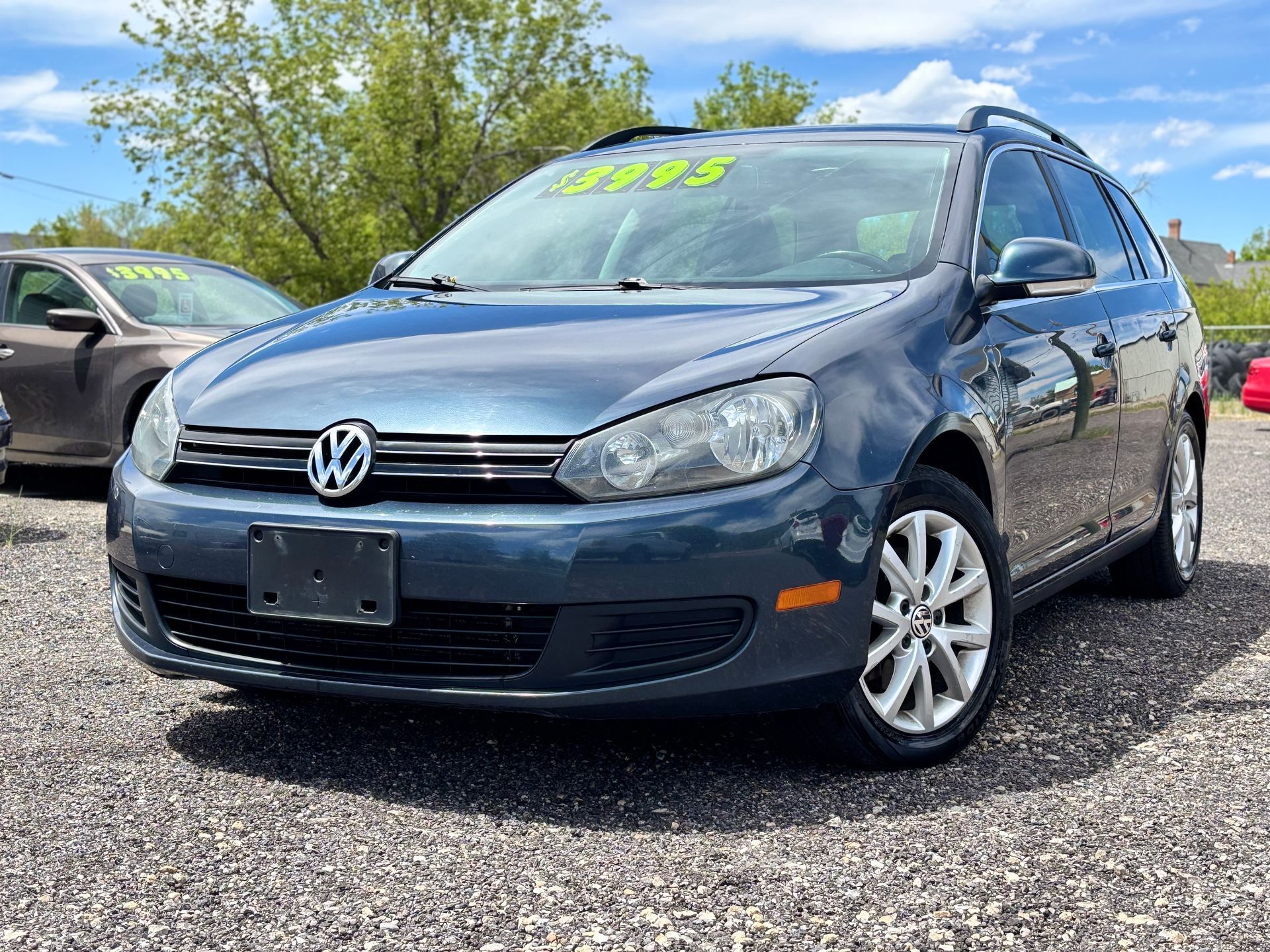 Dark blue Volkswagen hatchback parked outdoors on gravel, with price sticker on windshield.