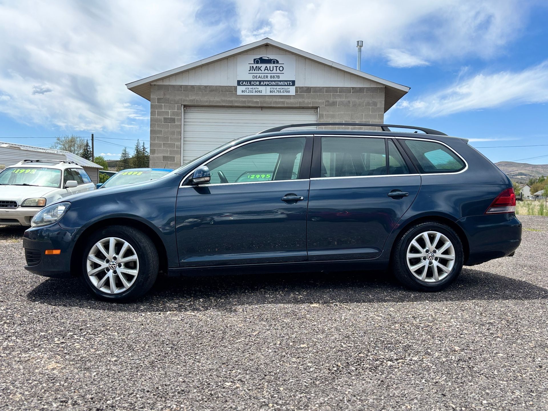 Dark blue station wagon parked in front of a small building under a partly cloudy sky.