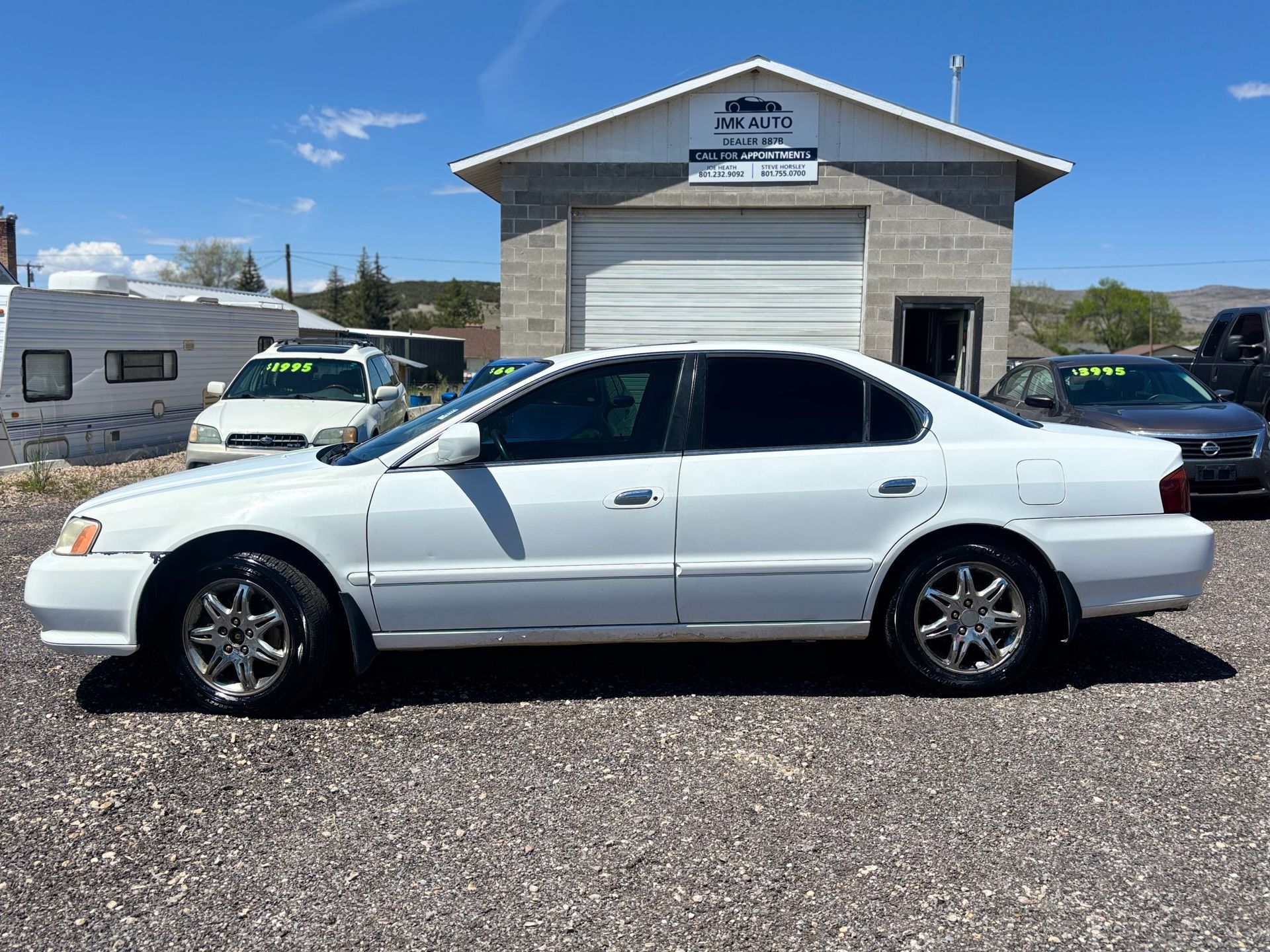White sedan parked in front of a small building on a gravel lot under a clear sky.