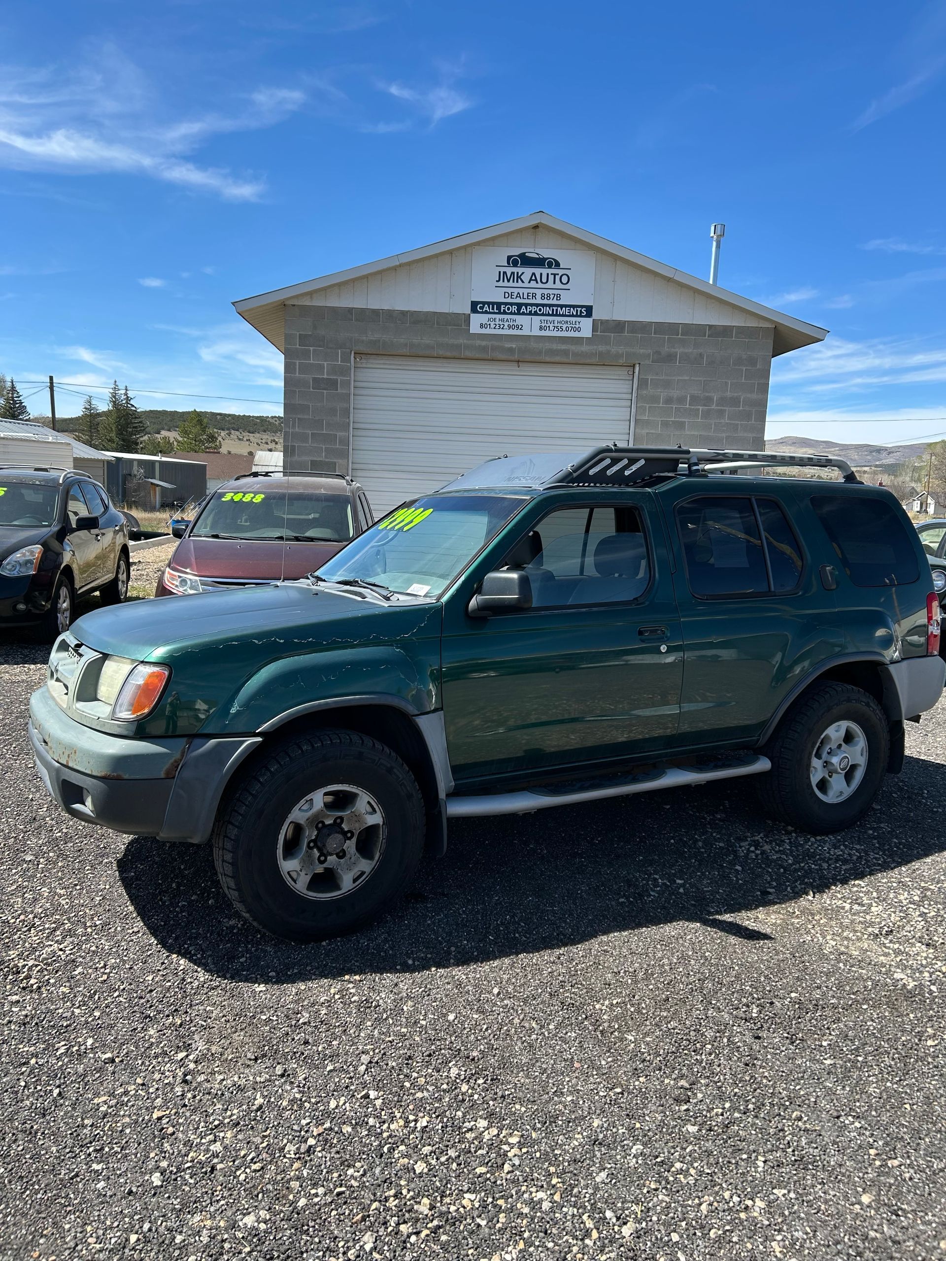 Green SUV parked on a gravel lot in front of a small building under a blue sky.