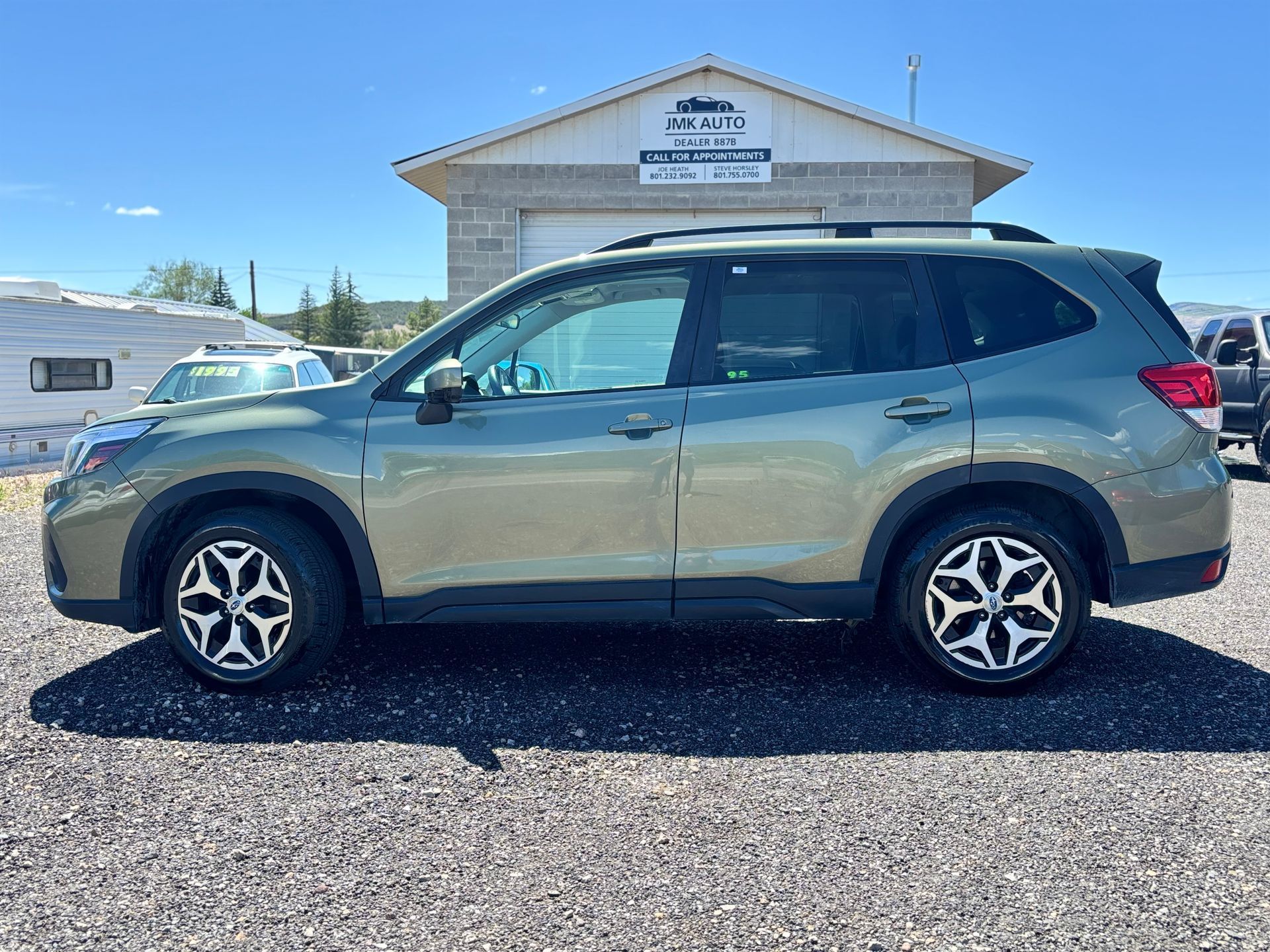 Side view of a beige SUV parked on gravel in front of a small building.